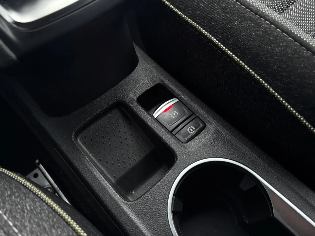 Gros plan sur la console centrale du Renault Captur 2025, montrant frein à main électrique et accoudoir tissu gris.