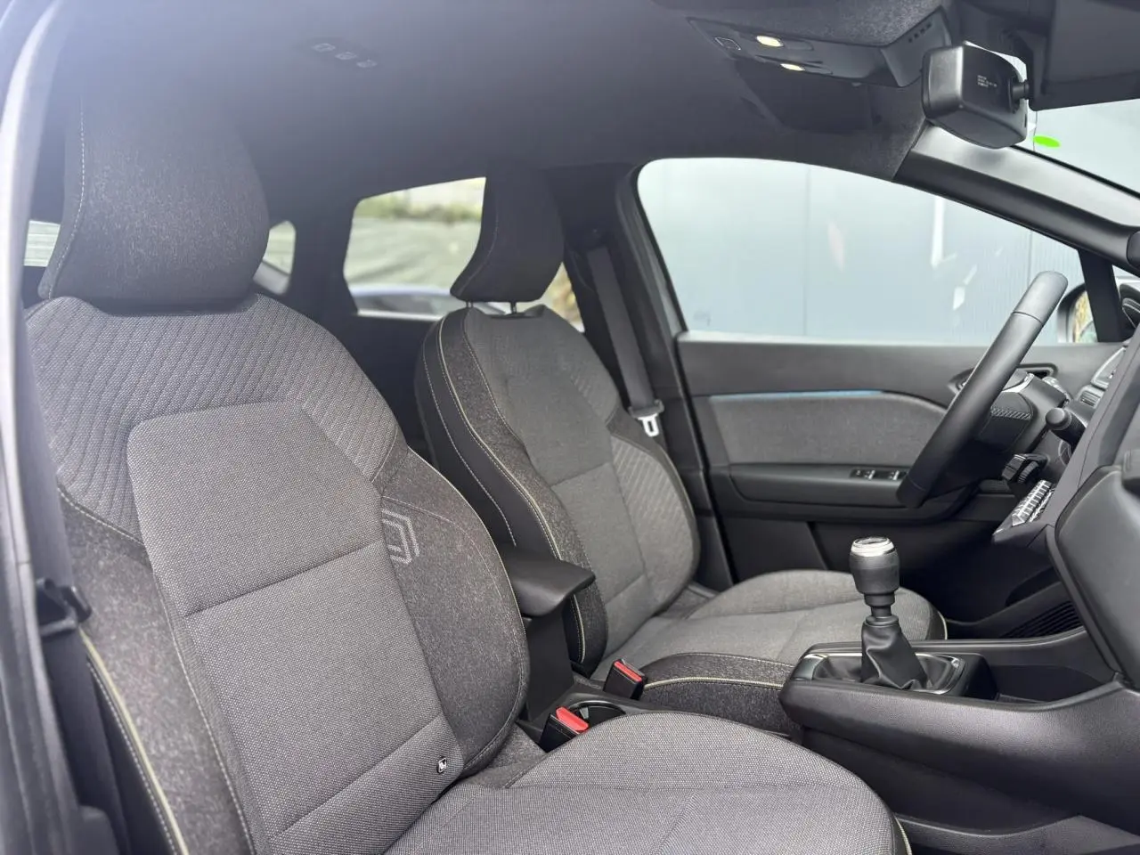 Vue intérieure côté conducteur du Renault Captur 2025, sièges gris avec coutures contrastées et levier de vitesses manuel.
