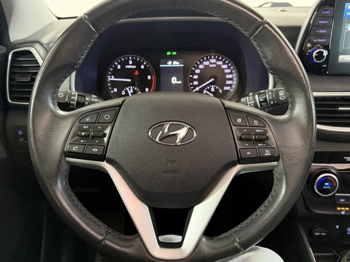 Vue rapprochée du volant en cuir noir du Hyundai Tucson 2019, avec commandes multifonctions et tableau de bord lumineux.