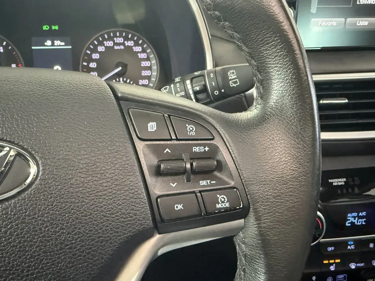 Gros plan sur le volant cuir noir du Hyundai Tucson 2019 avec commandes de régulateur de vitesse et tableau de bord partiel.