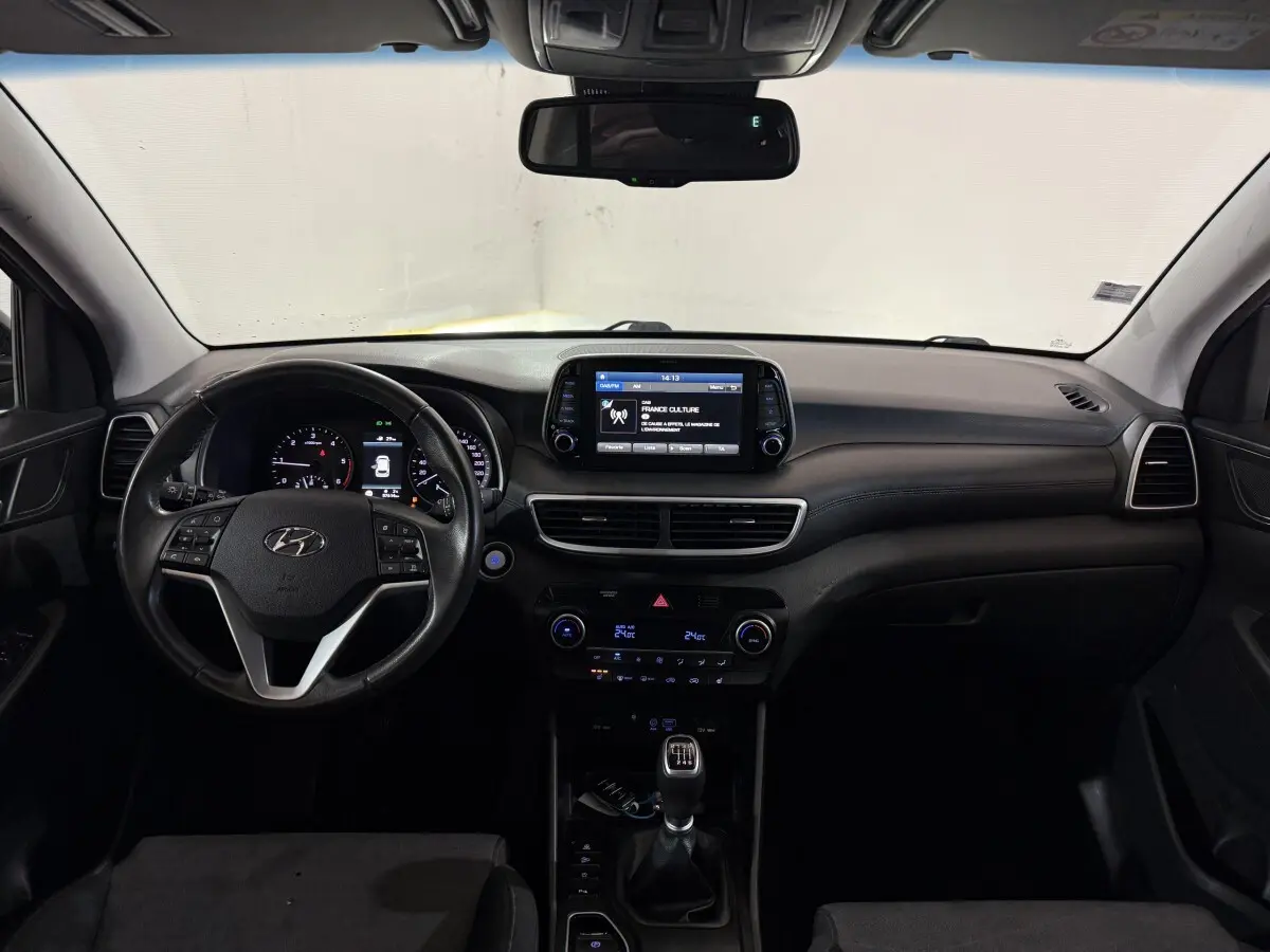 Vue intérieure avant du tableau de bord noir du Hyundai Tucson 1.6 CRDI avec écran tactile et volant multifonctions.