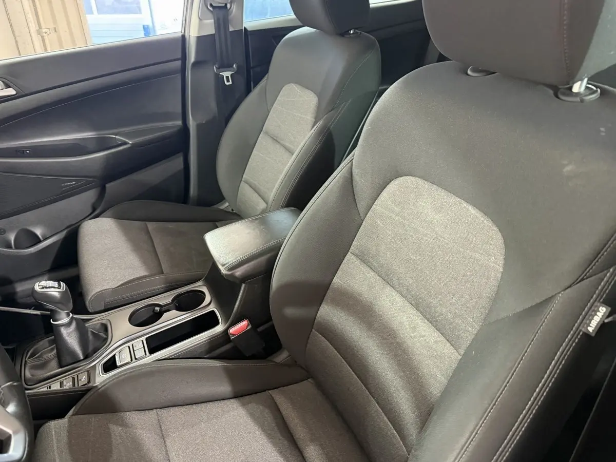 Vue intérieure côté conducteur du Hyundai Tucson 2019 noir, montrant sièges tissu et levier de vitesses manuelle.