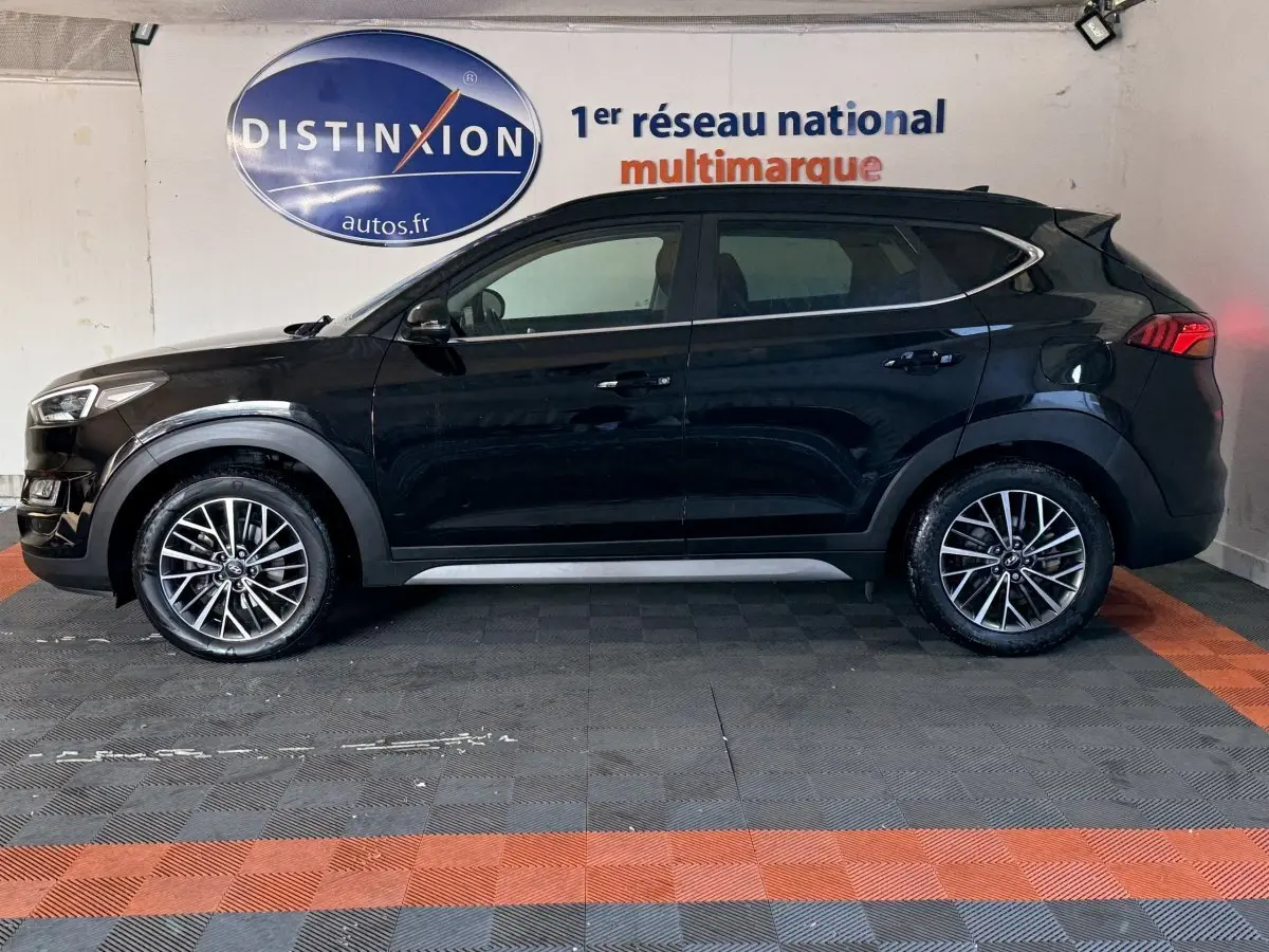 Vue latérale gauche d'un Hyundai Tucson noir 2019 avec jantes alliage et barres de toit noires en intérieur showroom.