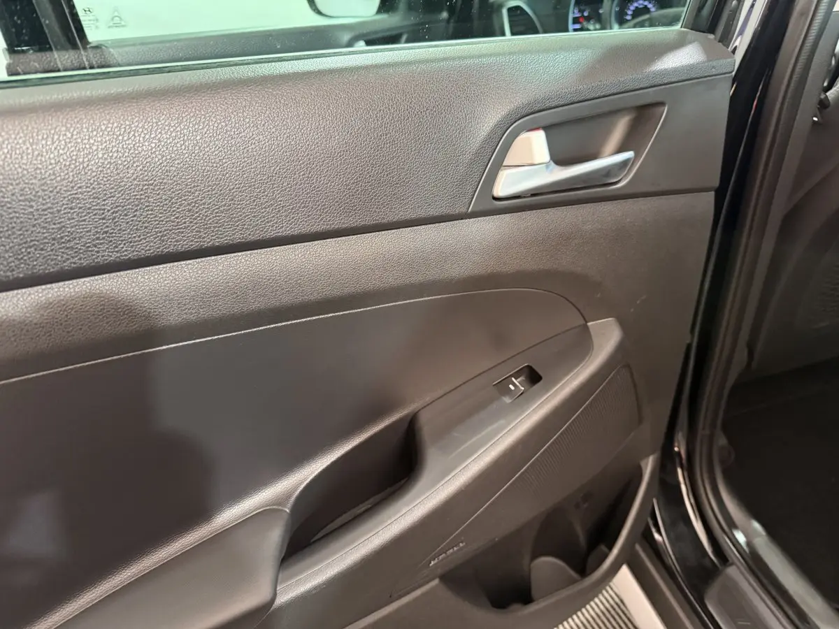 Vue rapprochée de la porte intérieure côté conducteur noire du Hyundai Tucson 2019, avec poignée argentée et commande de vitre.