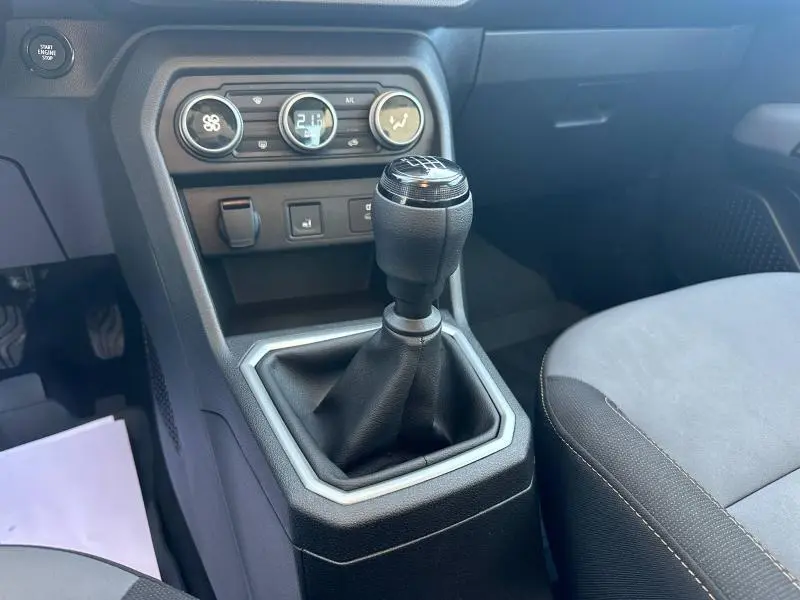 Gros plan sur la console centrale et levier de vitesses manuel du Dacia Sandero blanc, avec commandes climatisation et bouton start/stop.