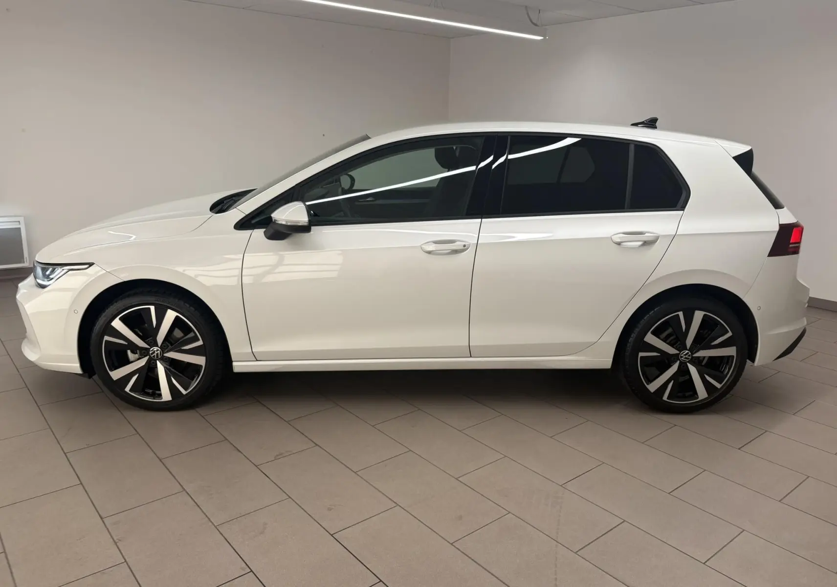 Vue de profil côté gauche d'une Volkswagen Golf 1.5 eTSI 116 BVM6 VW Edition blanche nacrée avec jantes alliage 18 pouces.