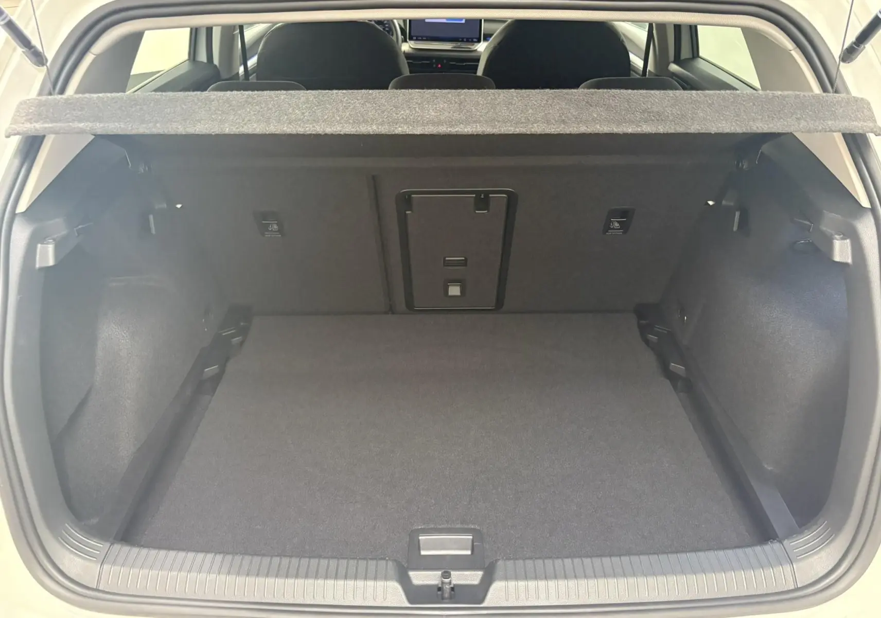 Vue du coffre ouvert d'une Volkswagen Golf 1.5 eTSI 116 BVM6 VW Edition blanc Oryx nacré, intérieur noir et tapis de sol.