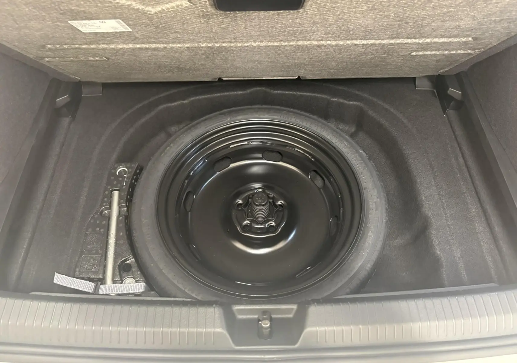 Vue plongeante sur la roue de secours noire et les outils dans le coffre du Volkswagen Golf 1.5 eTSI blanc Oryx nacré.