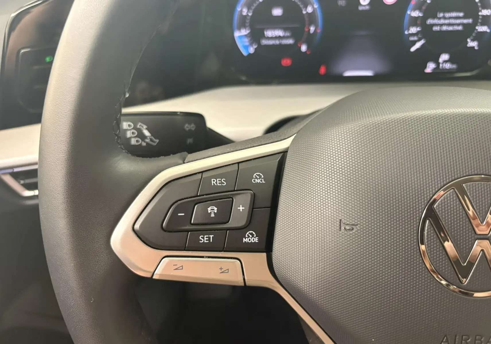 Gros plan sur le volant de la Volkswagen Golf 1.5 eTSI 2025, montrant les commandes de régulateur et le logo VW central.