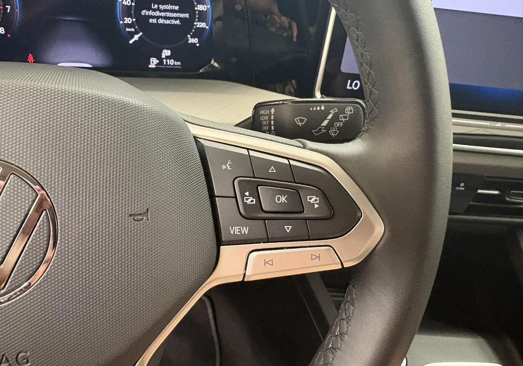 Gros plan sur le volant multifonction noir de la Volkswagen Golf 1.5 eTSI 2025 avec commandes intégrées et tableau de bord numérique.