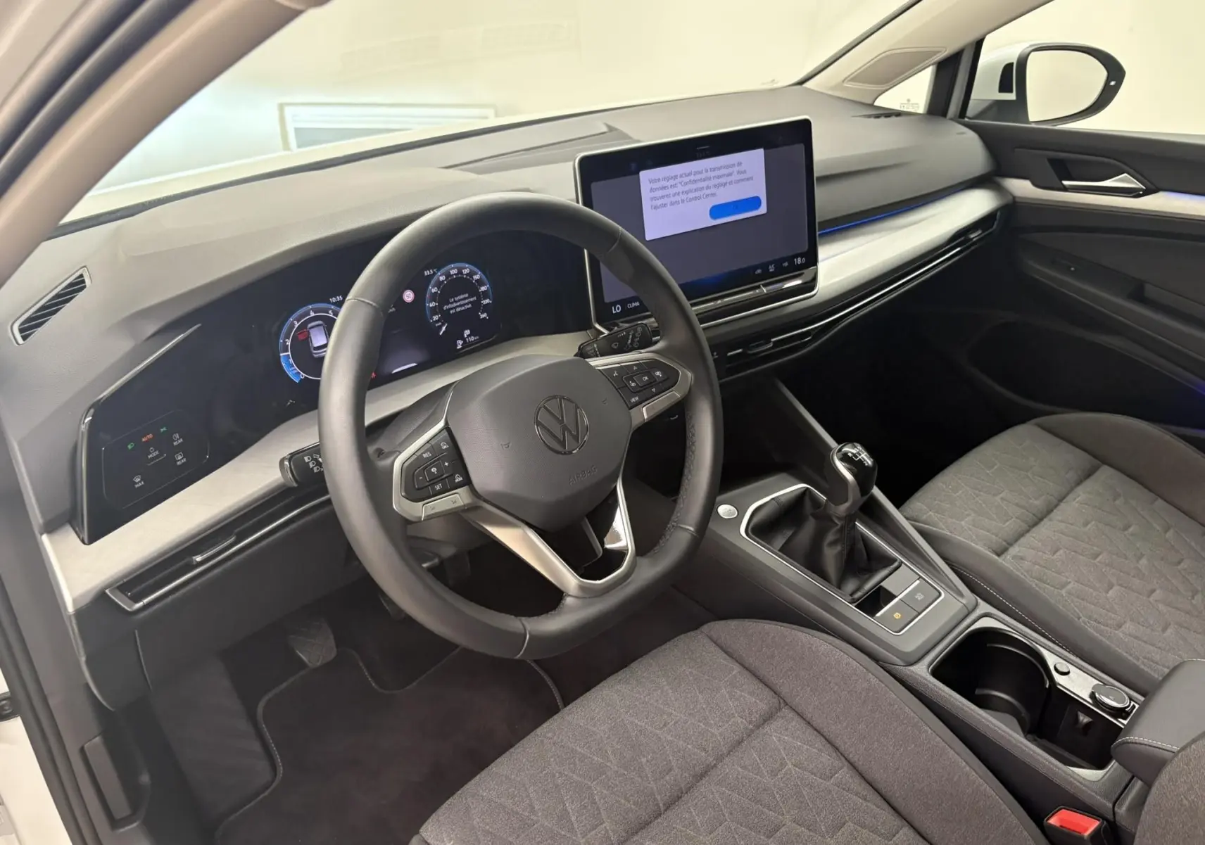 Vue intérieure côté conducteur de la Volkswagen Golf 1.5 eTSI 2025 avec tableau de bord numérique et boîte manuelle.