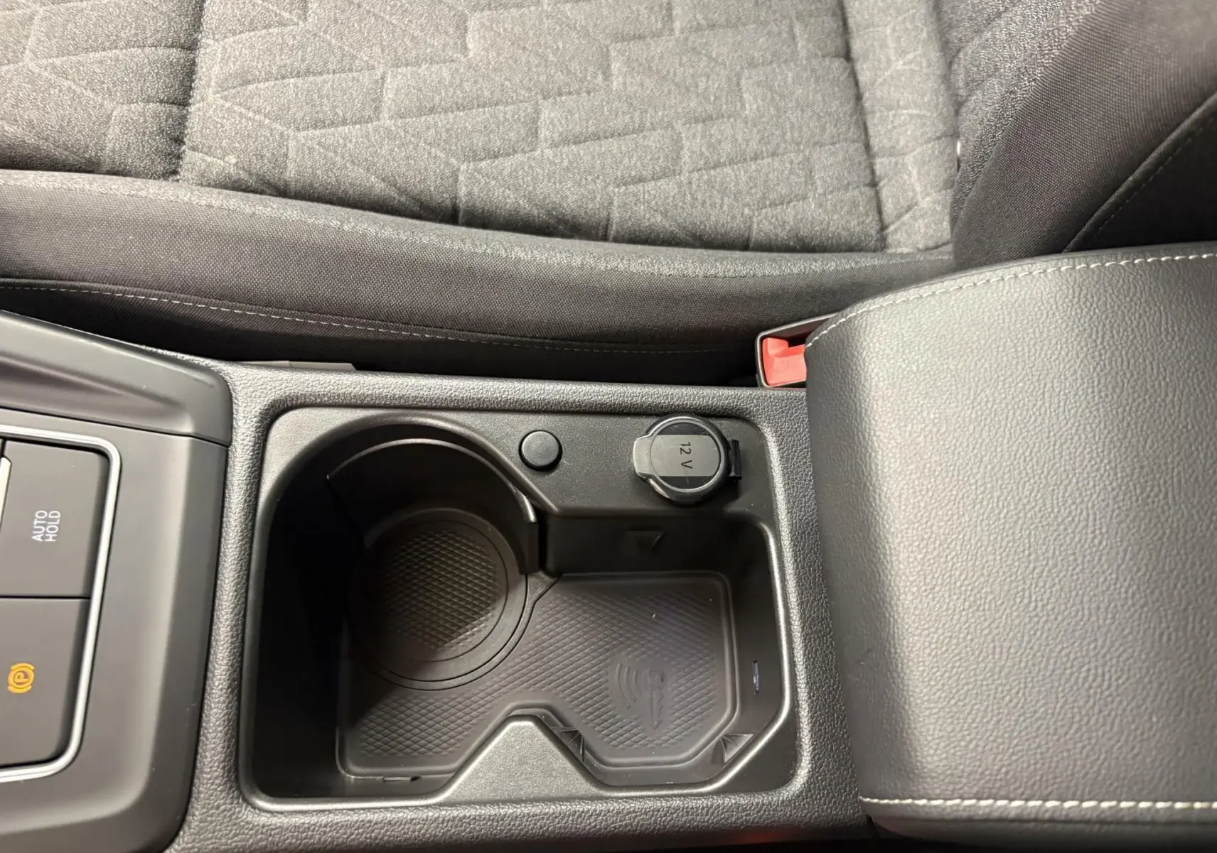 Gros plan sur la console centrale noire avec porte-gobelets, prise 12V et accoudoir en cuir gris de la Volkswagen Golf 2025.