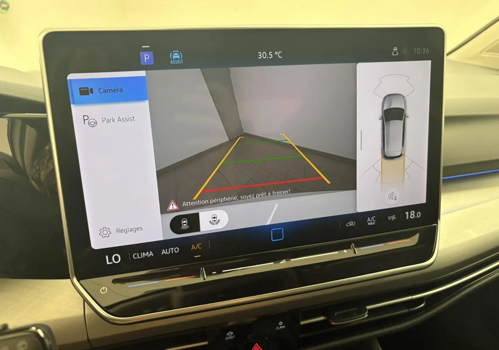 Écran tactile intérieur affichant la caméra de recul et l'assistance au stationnement d'une Volkswagen Golf Blanc Oryx nacré.