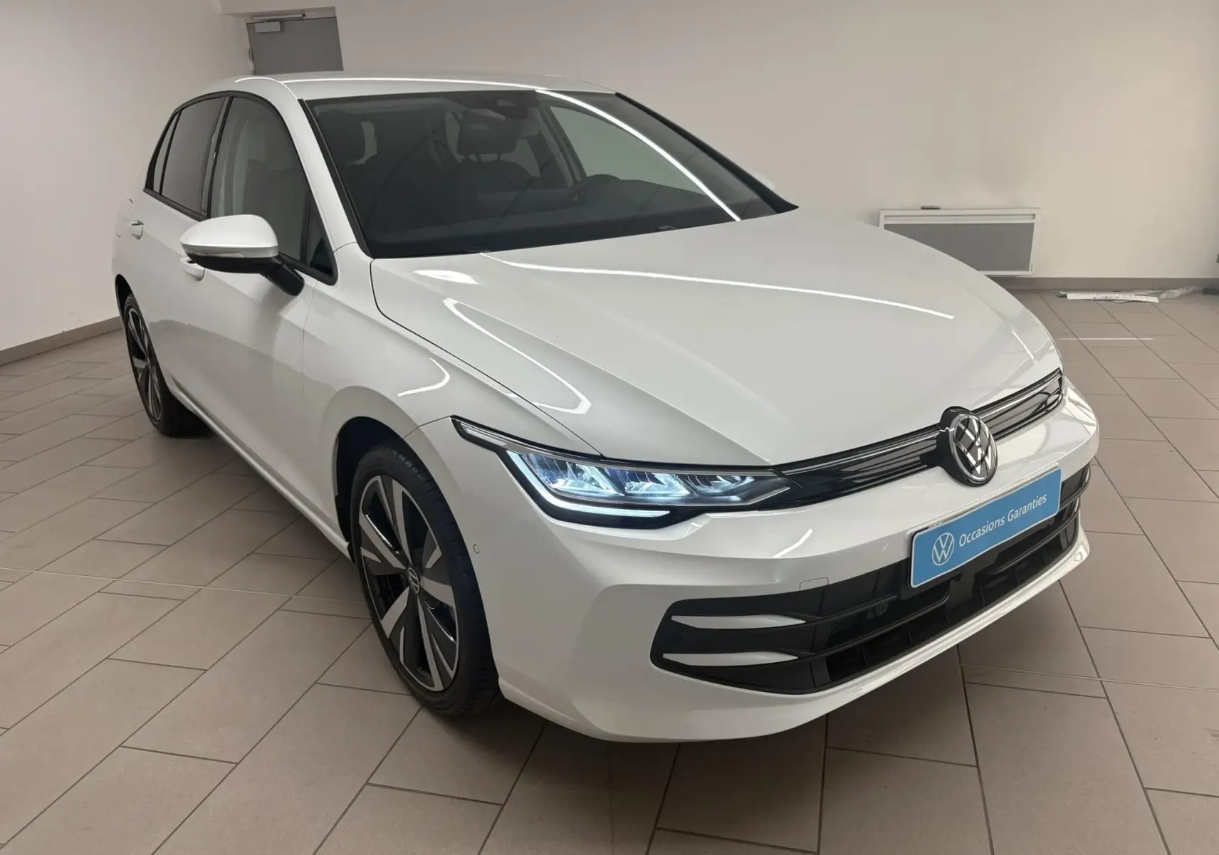 Volkswagen Golf 1.5 eTSI 2025 vue 3/4 avant en Blanc Oryx nacré avec jantes alliage 18'' Catania et phares LED allumés.