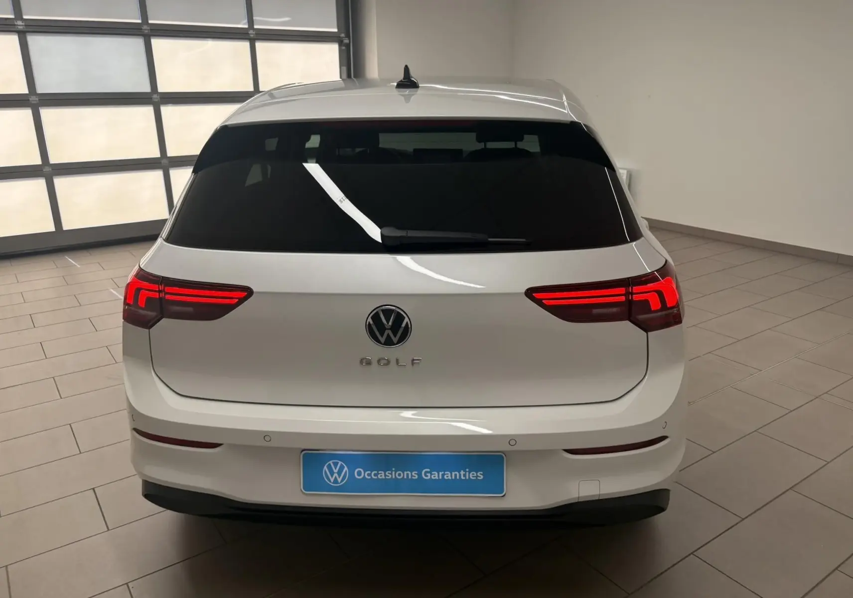Vue arrière d'une Volkswagen Golf 1.5 eTSI 2025 en blanc Oryx nacré avec feux LED allumés dans un intérieur showroom.