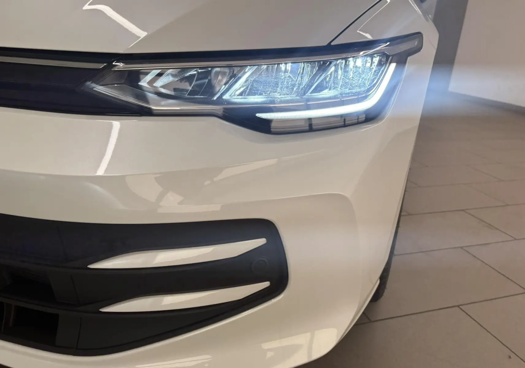 Gros plan sur le phare avant droit allumé d'une Volkswagen Golf 1.5 eTSI blanc oryx nacré, avec partie de la calandre visible.