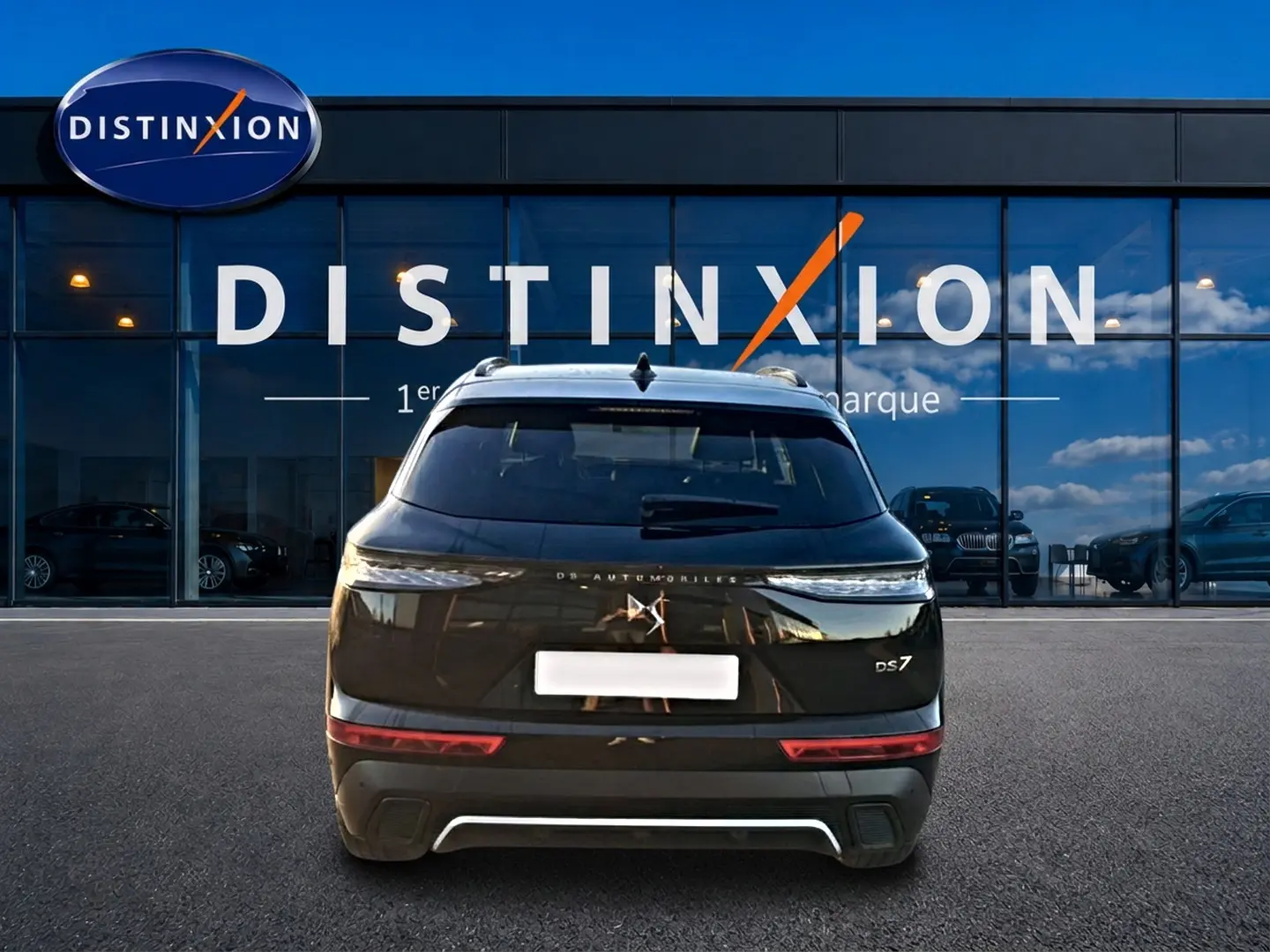 Vue arrière d'un DS7 noir 2026 avec feux LED fins et double sortie d'échappement, devant une vitrine Distinxion.