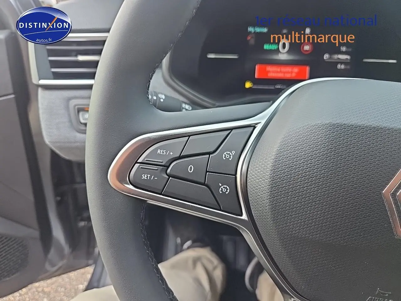 Gros plan sur les commandes multifonctions du volant de la Renault Clio V gris schiste, avec tableau de bord numérique en arrière-plan.