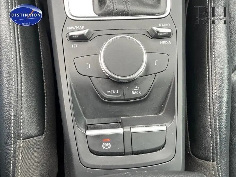 Gros plan sur la console centrale noire en cuir et plastique de l'Audi Q2 blanc Ibis, avec commandes multimédia et frein à main électrique.