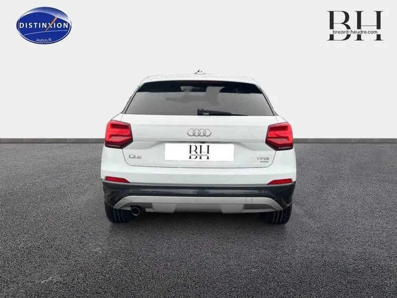 Vue arrière d'un Audi Q2 blanc Ibis avec vitres surteintées et feux arrière LED sur un sol gris.