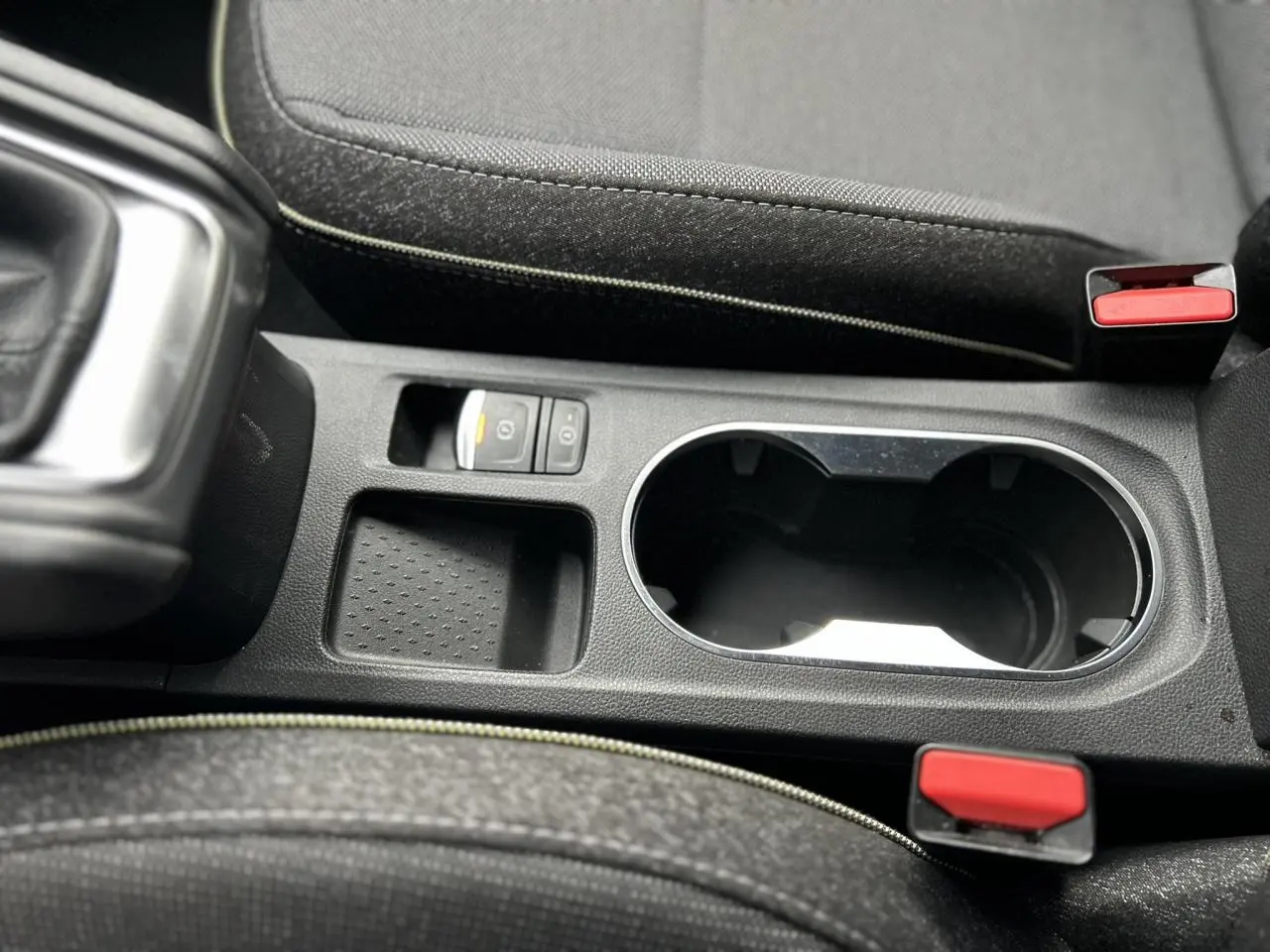 Gros plan sur la console centrale noire du Renault Captur 2025, avec porte-gobelets et bouton frein à main électrique.
