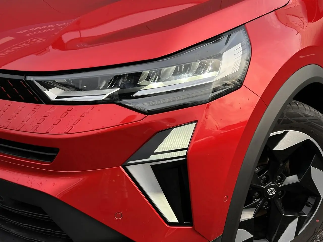 Gros plan sur l’avant droit du Renault Captur 2025 Rouge Flamme/Noir, mettant en valeur le phare LED et la jante alu noire diamantée.