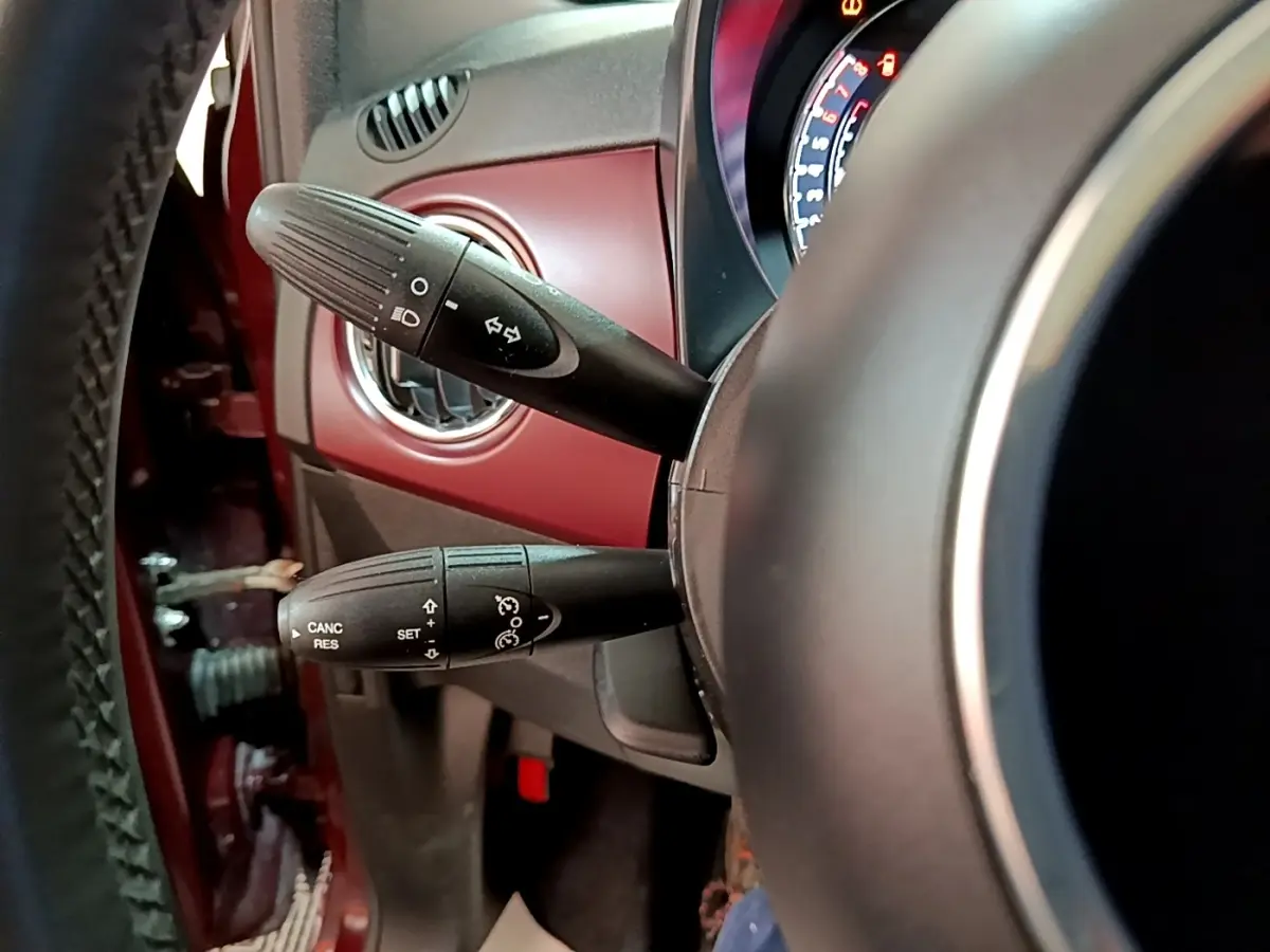 Gros plan sur la colonne de direction d’une FIAT 500 rouge, avec commandes de clignotants et régulateur de vitesse visibles.