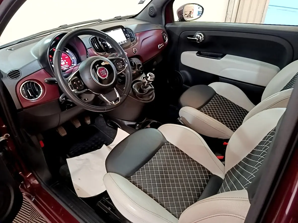 Vue intérieure côté conducteur de la Fiat 500 rouge, avec tableau de bord bordeaux et sièges bi-ton gris et noir.