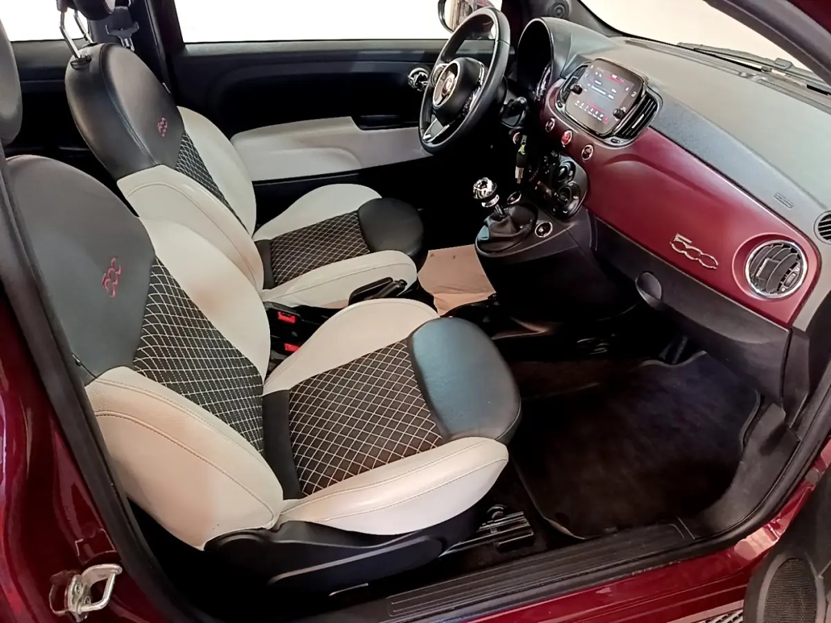 Vue intérieure côté conducteur de la Fiat 500 rouge, avec sièges bicolores et tableau de bord assorti rouge.