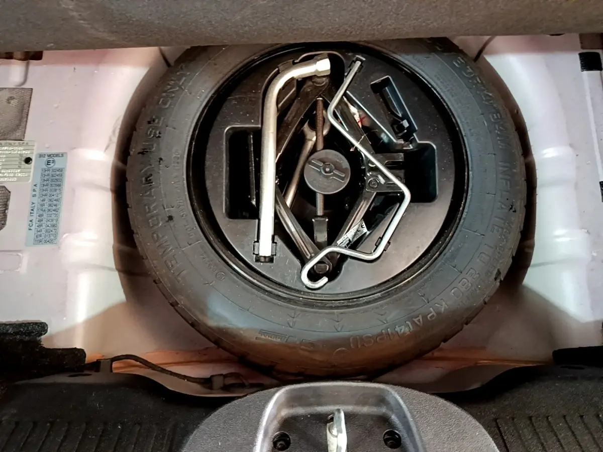 Vue rapprochée de la roue de secours et des outils de bord dans le coffre d'une FIAT 500 rouge.