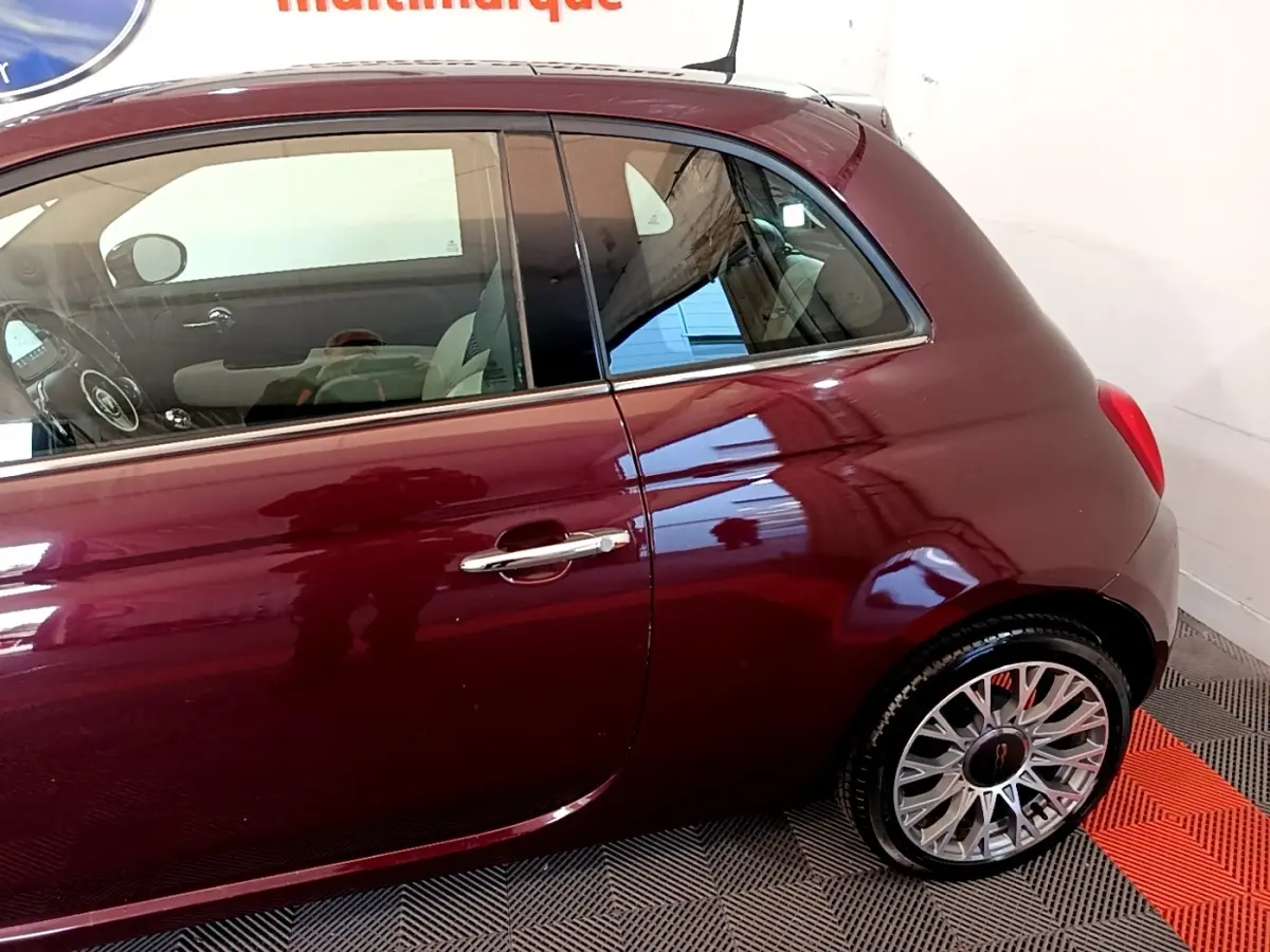 Vue côté droit arrière d'une FIAT 500 rouge bordeaux avec jantes alliage et poignée de porte chromée.