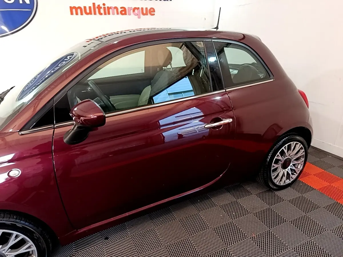 Vue latérale gauche d'une FIAT 500 rouge bordeaux, mettant en valeur la porte et la jante alliage au design complexe.