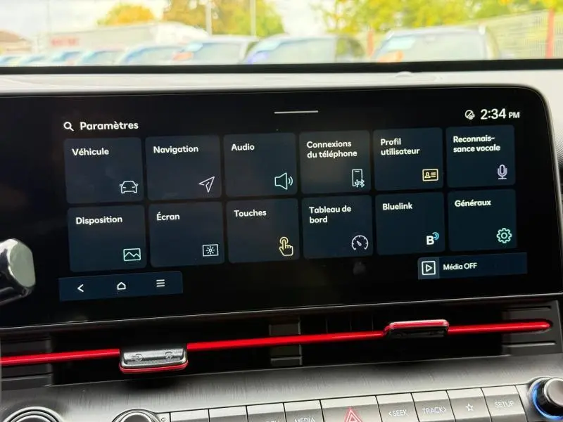 Écran tactile central du Hyundai Kona 2025 affichant le menu des paramètres, avec bandeau rouge décoratif sous l'écran.