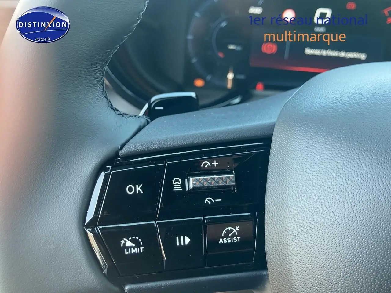 Gros plan sur les commandes au volant de l'Alfa Romeo Junior 1.2 hybride ivoire et noir, affichage digital en arrière-plan.