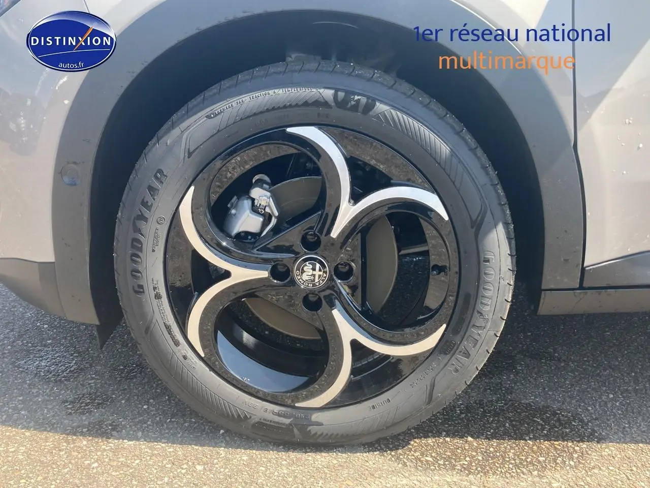 Gros plan sur la jante en alliage noire et ivoire de l'Alfa Romeo Junior 1.2 hybride, avec pneu Goodyear visible.