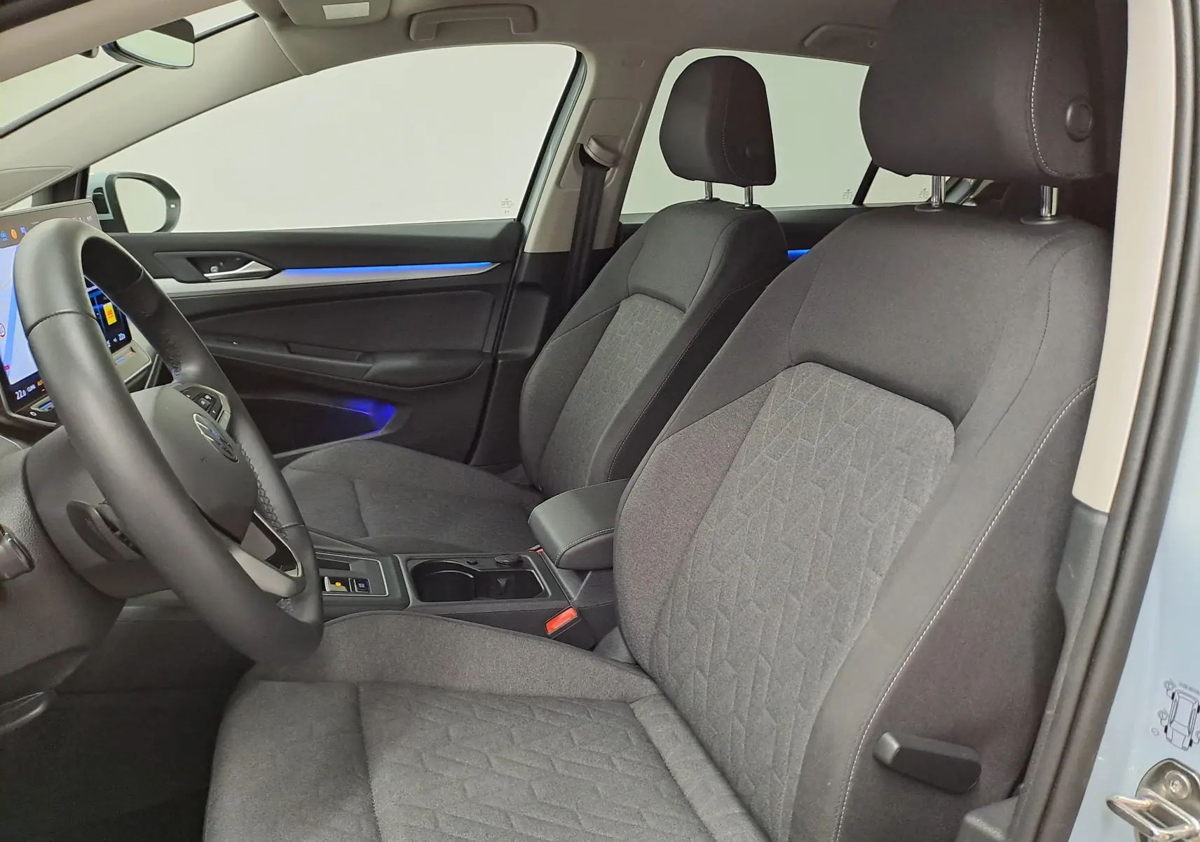 Vue intérieure côté conducteur de la Volkswagen Golf 1.5 eTSI 2025, sièges tissu gris avec éclairage d'ambiance bleu.