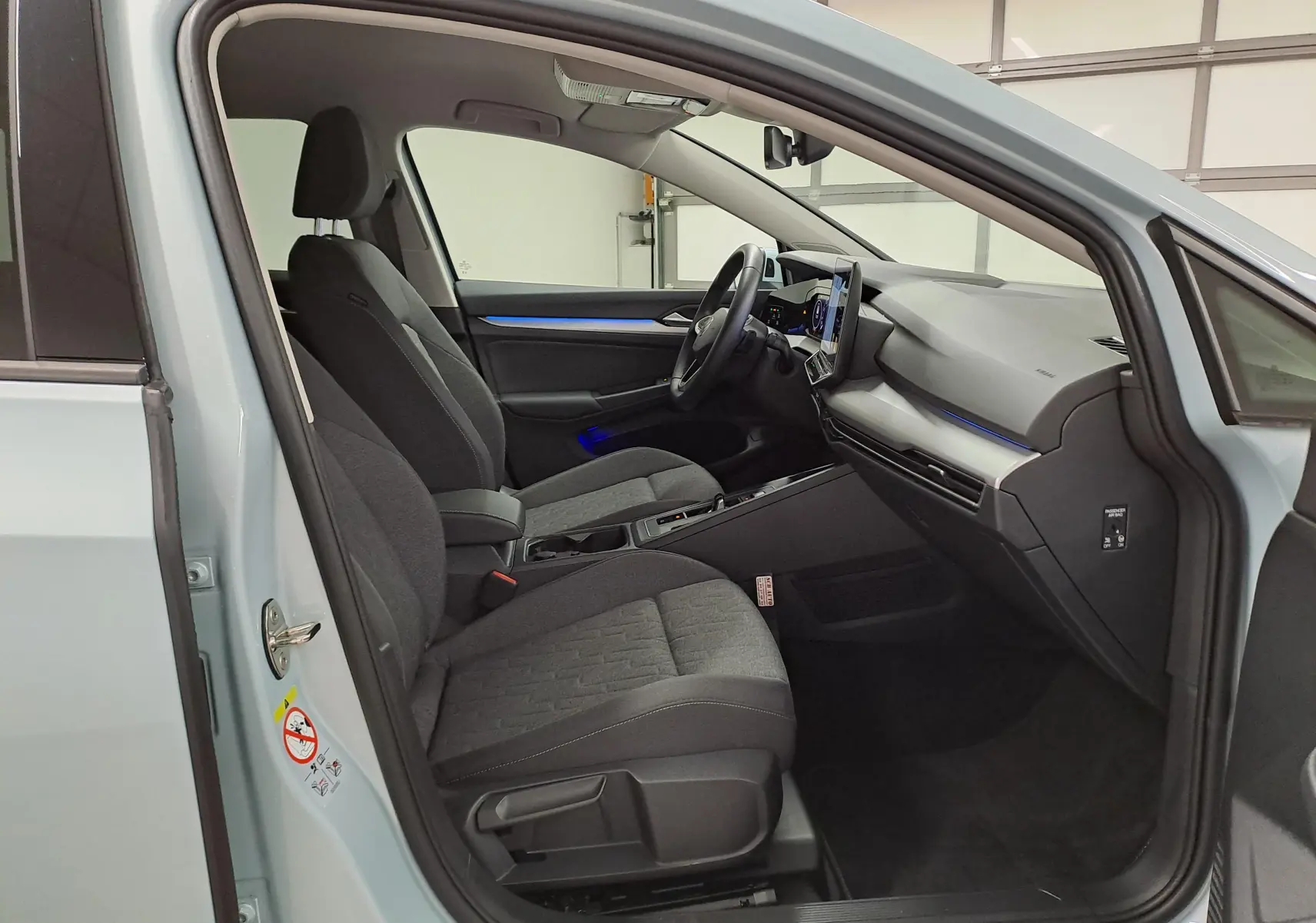 Vue intérieure côté conducteur de la Volkswagen Golf 1.5 eTSI 2025 en Bleu Glacier, avec sièges tissu gris et tableau de bord moderne.