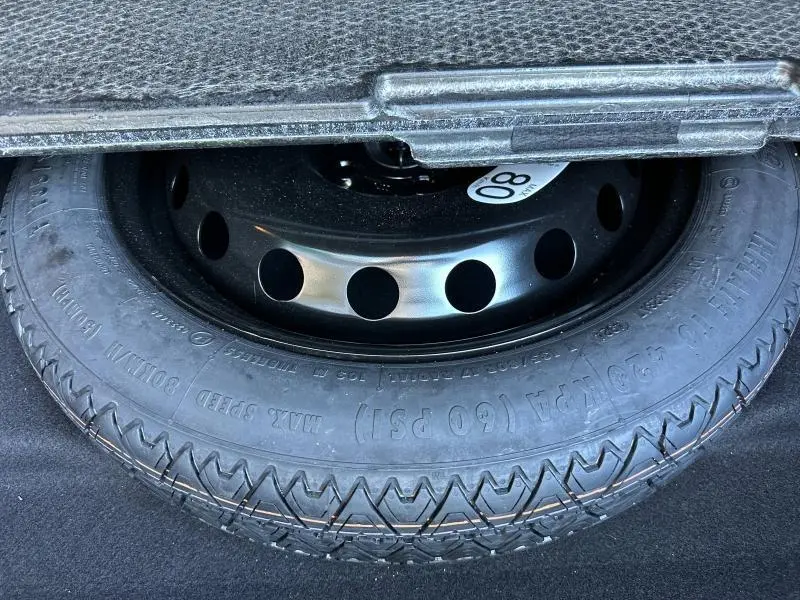 Gros plan sur la roue de secours noire en acier dans le coffre d'une Renault Symbioz rouge.