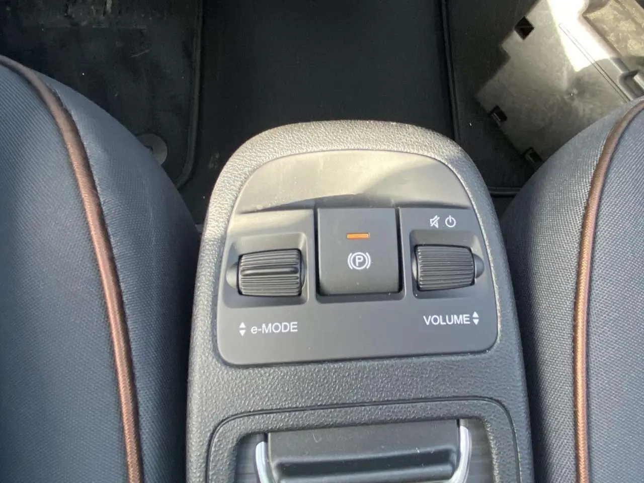 Gros plan sur la console centrale entre les sièges avant en tissu noir avec surpiqûres marron de la Fiat 500 Electrique noire.