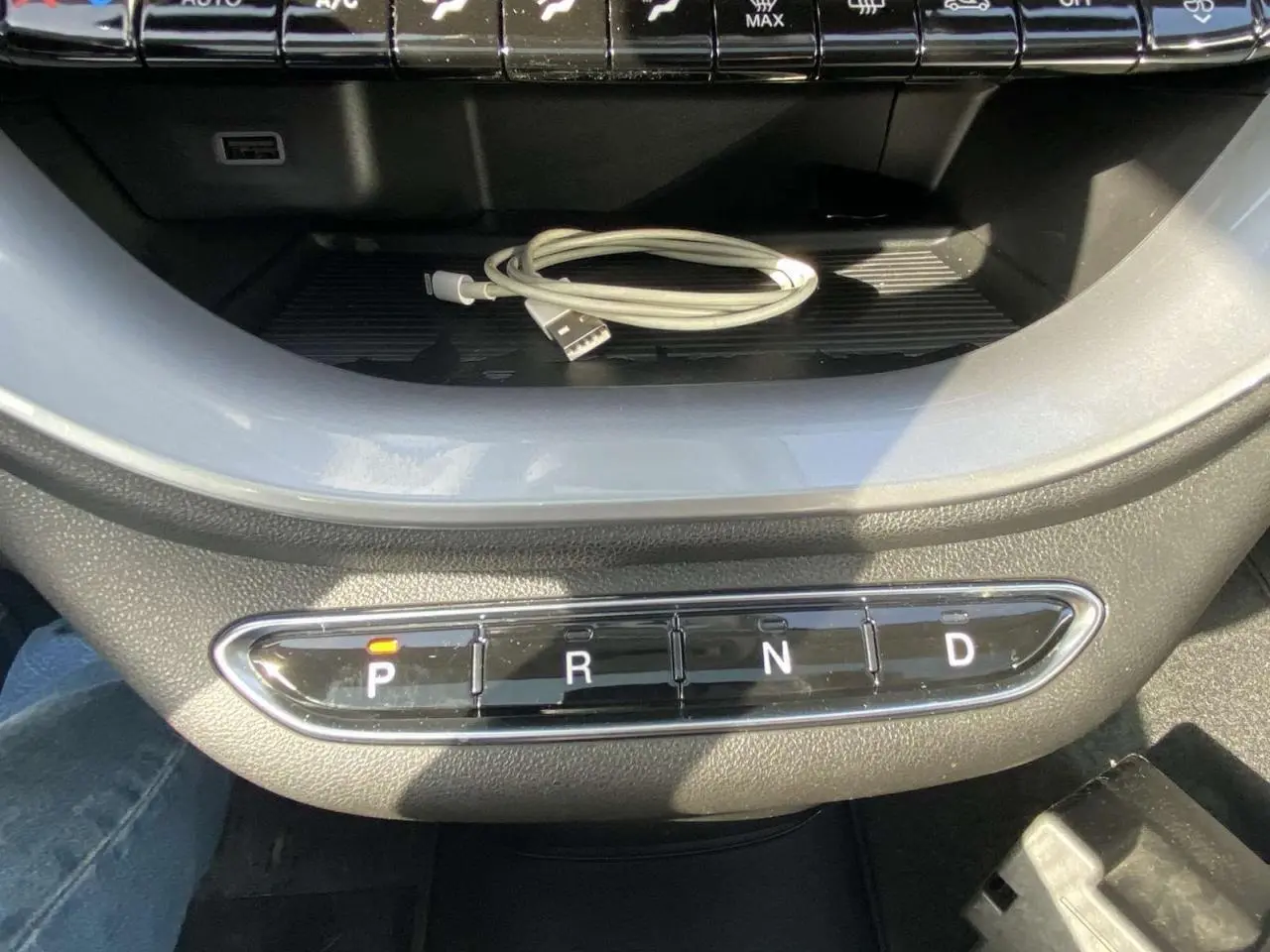 Gros plan sur la console centrale de la Fiat 500 électrique noire, avec les boutons de la boîte auto et un câble USB posé dessus.