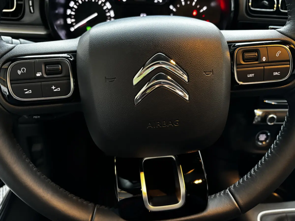 Gros plan sur le volant multifonctions noir avec logo chromé Citroën et commandes intégrées du tableau de bord C3 2024.