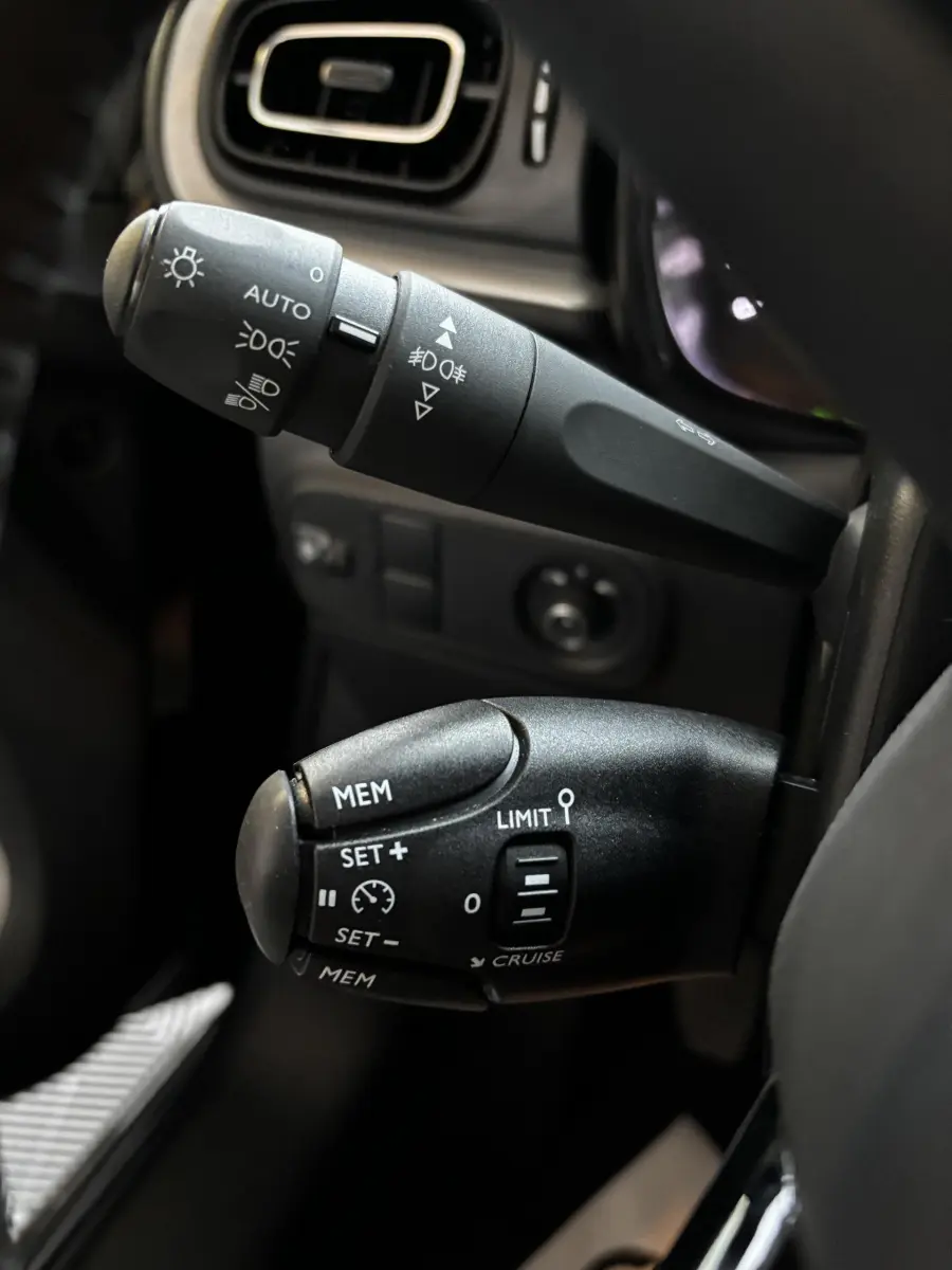 Gros plan sur les commandes au volant noir de la Citroën C3 2024, mettant en valeur les réglages des phares et du régulateur de vitesse.