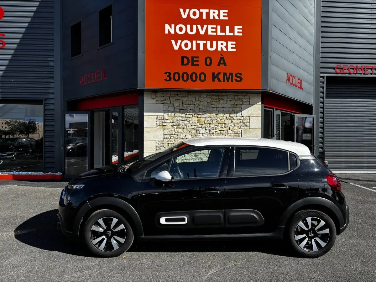 Profil côté gauche d'une Citroën C3 2024 bicolore noir et toit blanc, avec protections latérales caractéristiques.