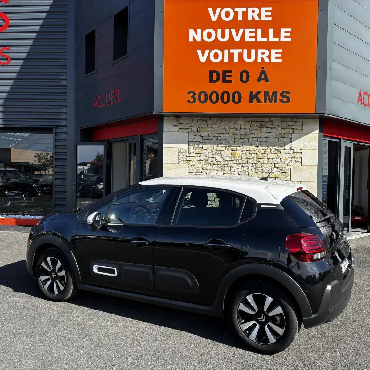 Vue 3/4 arrière droite d'une Citroën C3 noire à toit blanc avec protections latérales blanches, stationnée devant un bâtiment.