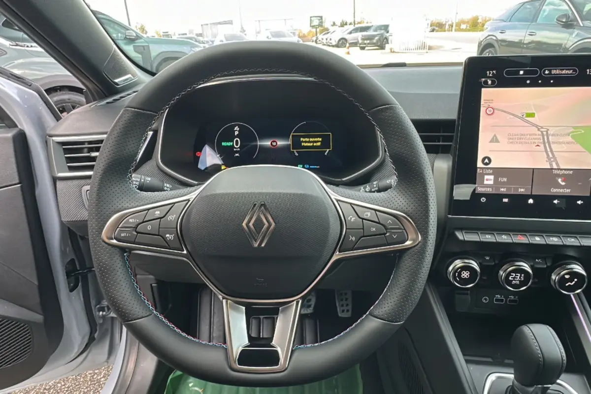 Vue intérieure centrée sur le volant cuir multifonctions d’une Renault Clio gris rafale avec écran tactile et tableau de bord numérique.