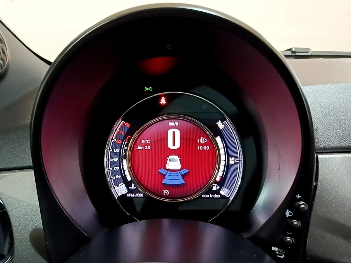 Gros plan sur le tableau de bord numérique circulaire de la Fiat 500 Hybrid avec affichage rouge et indicateurs blancs.