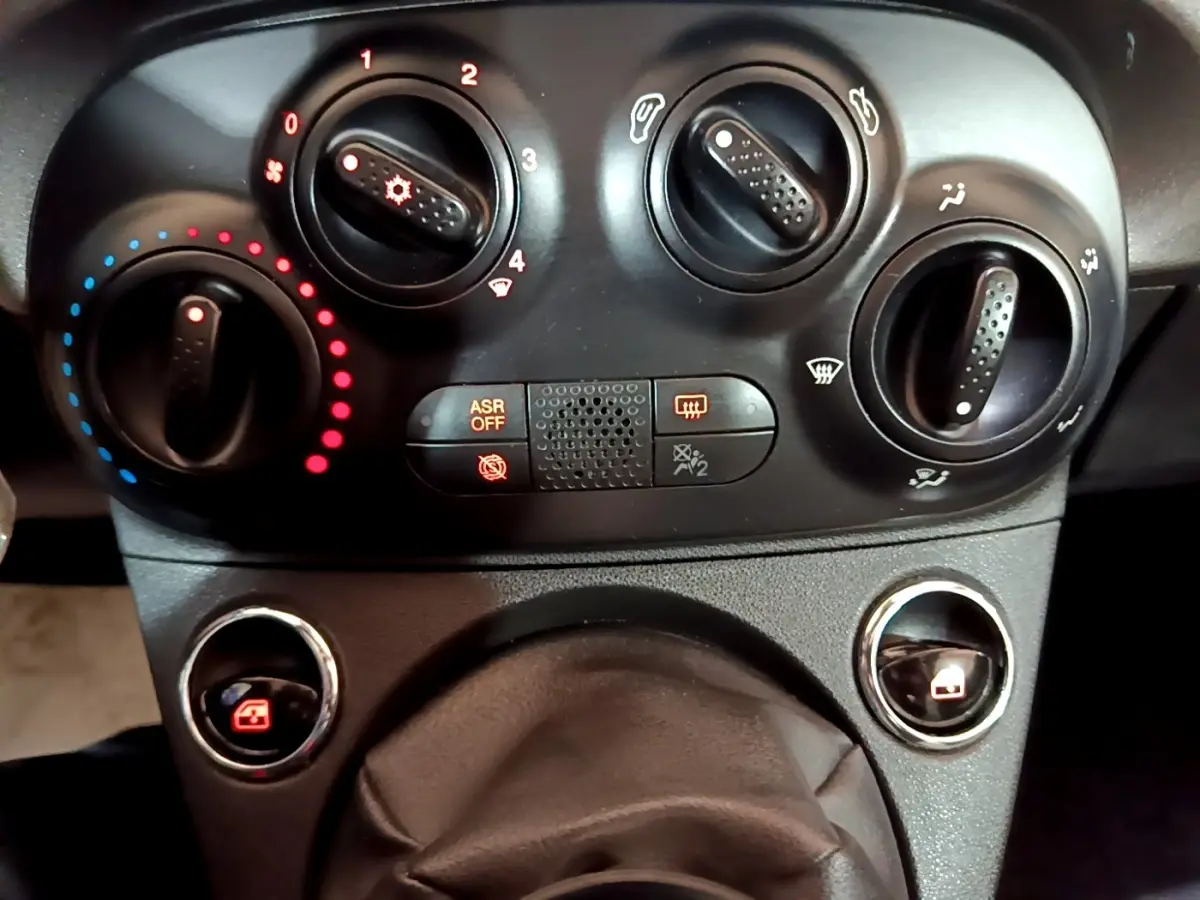 Gros plan sur les commandes de climatisation et vitres électriques d’une Fiat 500 gris foncé, tableau de bord noir.