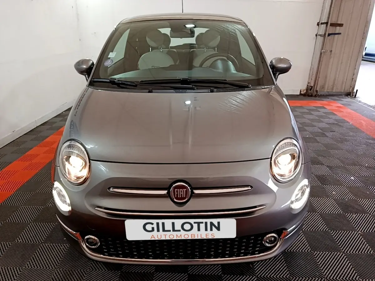 Vue avant d'une Fiat 500 gris foncé avec phares allumés dans un garage fermé.