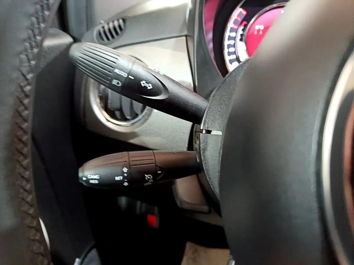 Gros plan sur les commandes au volant cuir de la FIAT 500 Hybrid gris foncé, avec tableau de bord partiellement visible.