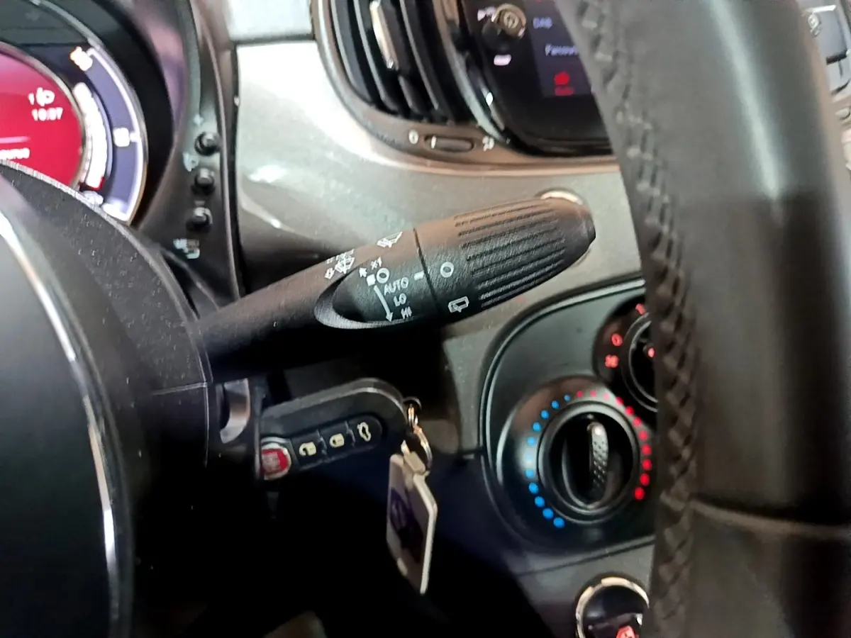 Détail du volant cuir et commandes de climatisation d'une Fiat 500 hybride gris foncé, vue côté gauche.